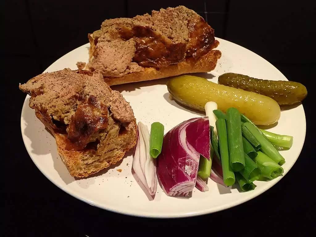 Hot 'leverpostej' on toasted, buttered rye bread on a white plate with accompaniment (red and spring onions and green pickled gherkins)