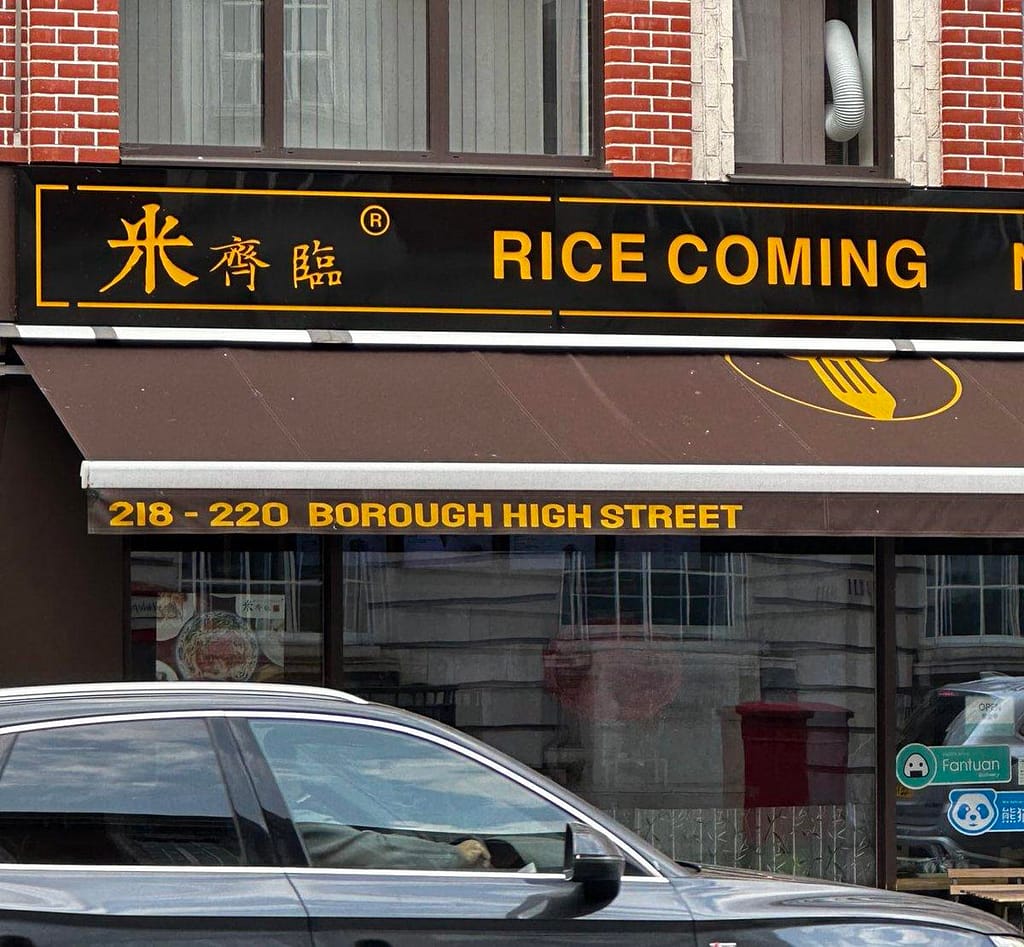 The restaurant is called Rice Coming and it and its address in Borough High St are in orange with orange Chinese characters on a marroon awning over the tope of the shop. A black SUV (no idea make & model, who cares TBH) is in front.