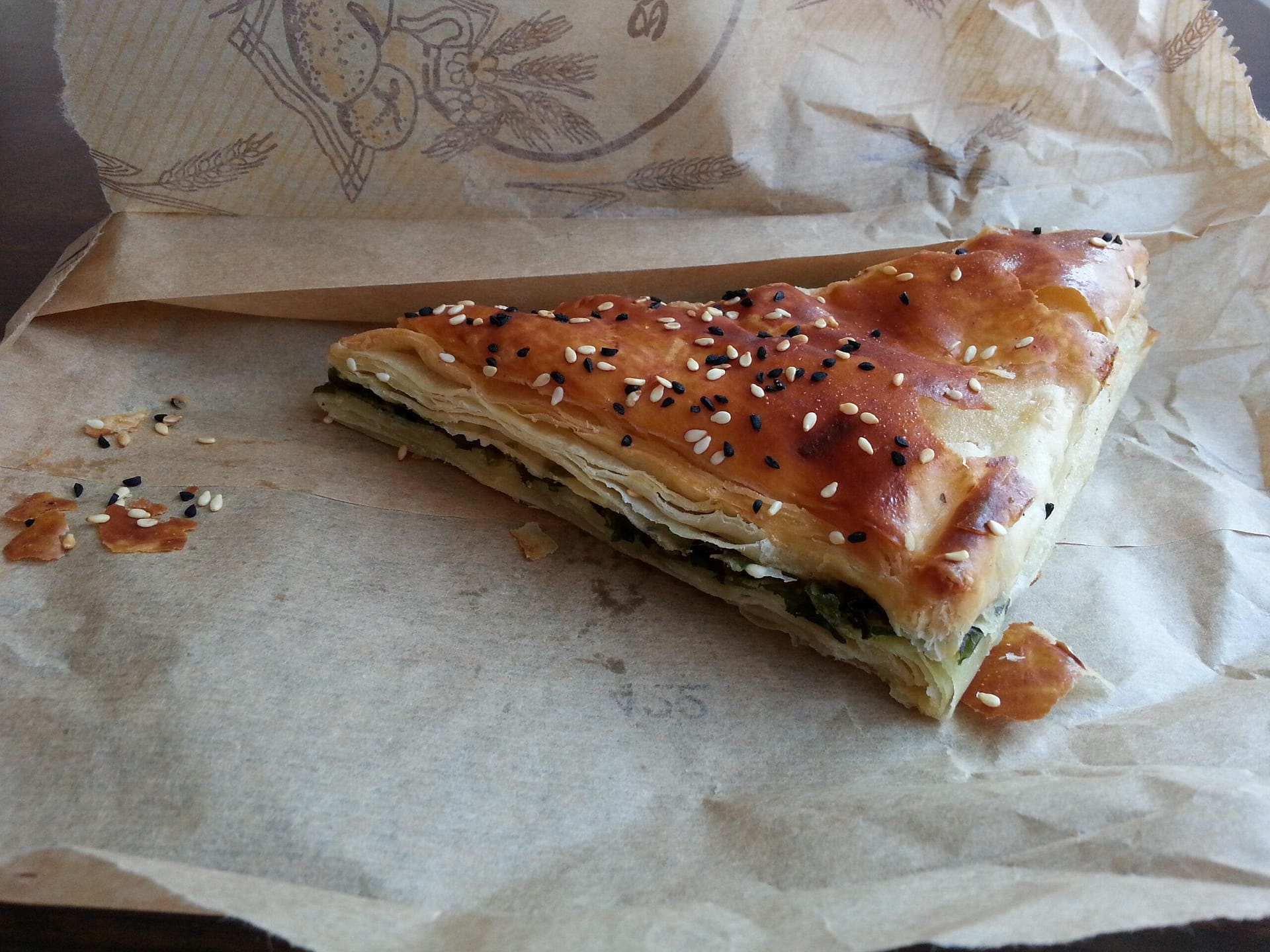 Triangles of dark brown, crispy pastry, with black & yellow sesame seeds scattered on the top, resting on a paper bag.