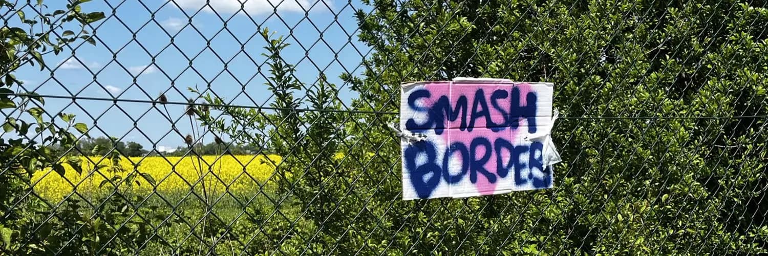 A sign saying "smsh borders" on a white sheet hangs off a chain-link fence.